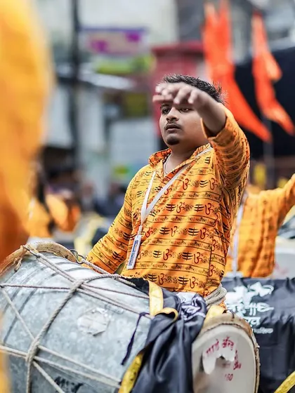 A dhol player signals to the group, his expression focused and intense amidst the orange-clad crowd.