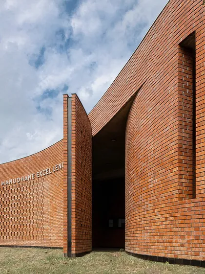 The entrance to a building at the Dakshana Institute in Pune features a curved brick wall with a perforated pattern. The use of local materials and craftsmanship creates a strong sense of place and connection to the region.