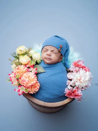 A beautifully simple newborn portrait. The baby is swaddled in blue and placed in a basket adorned with flowers, creating a serene and artistic image against a matching blue background.
