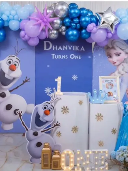 An elaborate Frozen-themed first birthday stage, featuring character cut-outs, marquee letters spelling "ONE," and a detailed balloon arch.