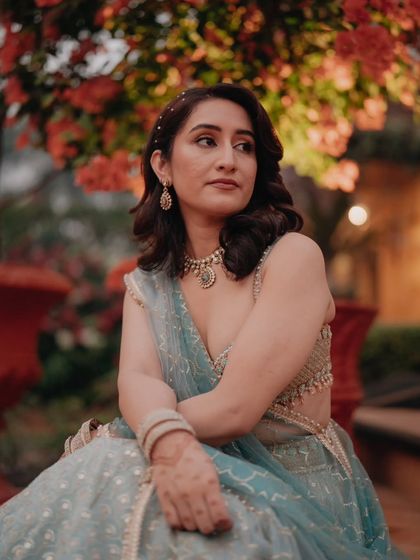 A beautiful portrait of the bride sitting amidst lush greenery, her thoughtful expression captured in the soft evening light.