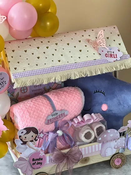 The full view of the fairy-themed baby girl trolley hamper. It's decorated with a heart-print canopy, a plush star pillow, and a 'Bundle of Joy' sign.