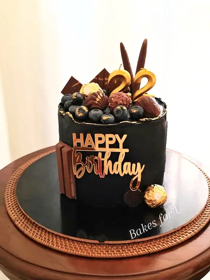 A sophisticated black cake loaded with goodies. This Belgian chocolate cake is topped with blueberries, Ferrero Rocher, KitKats, and other chocolate treats.