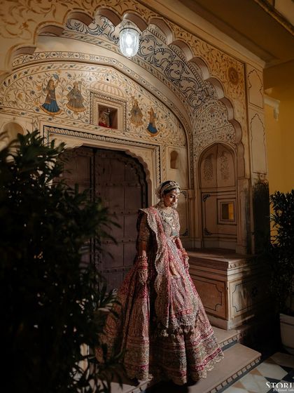 A full-length bridal portrait of Aashi in front of an intricately carved palace doorway.