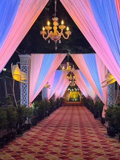 A soft and dreamy wedding entranceway designed with pastel pink and blue drapes. The gentle lighting from the chandeliers and the lotus-shaped floor lamps add a touch of magic, welcoming guests into a world of elegance.