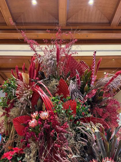 A closer look at the Christmas arrangement, showcasing the intricate layering of textures. King protea flowers, painted palm leaves, and red berries come together to create a rich, festive tapestry.