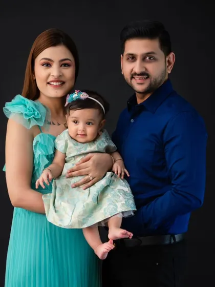 A formal family portrait against a solid black background. The family's coordinated blue and teal outfits create a rich, jewel-toned image that is both elegant and striking.