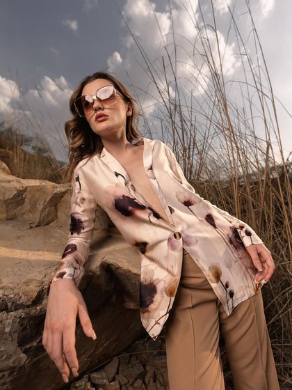 This low-angle shot makes the outfit appear powerful and statuesque. The composition uses the rocks and grass to frame the model, emphasizing her presence in the landscape.