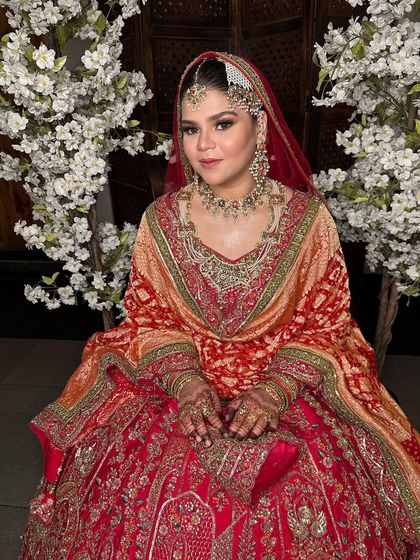 A full view of this beautiful bride in her red and orange lehenga. The makeup is designed to harmonize with the warm tones of her outfit, creating a cohesive and stunning bridal appearance.