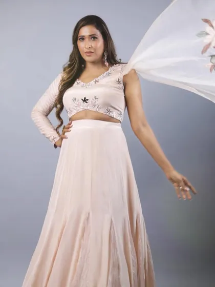 A perfect choice for a bridesmaid or a sangeet, this pastel godet lehenga flows beautifully. The design features a unique one-sided trail sleeve and delicate appliqué work on the blouse, offering a soft, modern, and romantic silhouette.