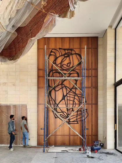 An abstract metal sculpture being installed on a wooden paneled wall. This piece demonstrates our approach to line art in a three-dimensional form, creating a dynamic interplay of shadow and form.