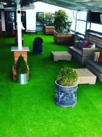 A rooftop lounge area completely covered in artificial grass. This surface is perfect for commercial spaces like cafes and bars, providing a comfortable and attractive floor for guests.