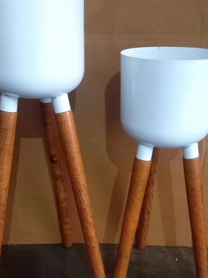 A set of two modern tripod planters. These feature clean white metal pots on sturdy, polished wooden legs, perfect for a Scandinavian or mid-century modern interior style.