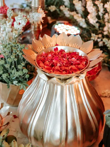 The warm glow of lights reflecting on the brass lotus urn, adding to the rich and inviting ambiance of the traditional event.