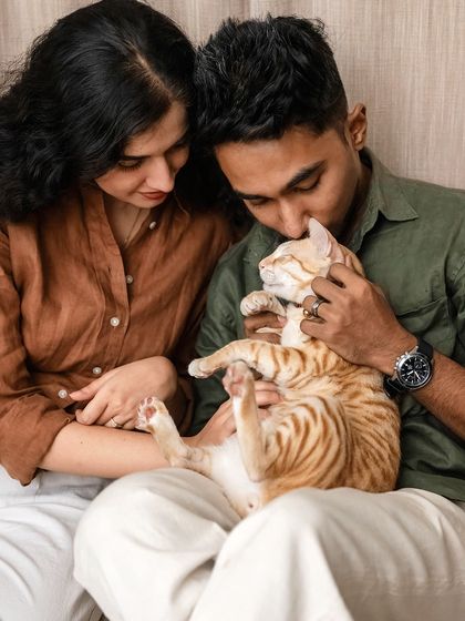 A tender moment where a couple lovingly cradles their orange cat, Toffee, during their at-home engagement shoot. A perfect picture of a happy family.