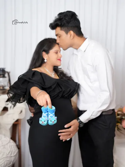 A creative gender reveal pose in our studio, with the couple holding tiny blue baby shoes.