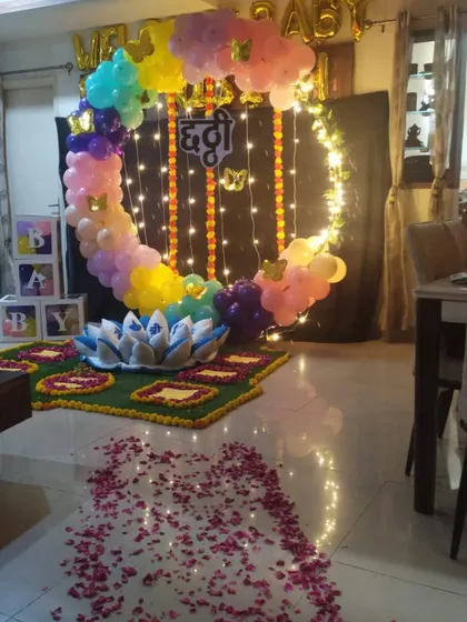 A beautiful Chhatthi ceremony setup with a mix of traditional and modern elements. The decoration includes a circular balloon arch with fairy lights, "Welcome Baby" foil balloons, and a floor decorated with flower petals.
