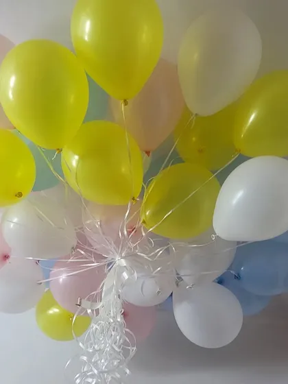 A bunch of pastel-colored helium balloons, including yellow, pink, and blue.