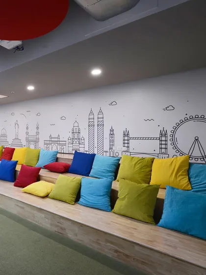 Amphitheater-style seating with colorful cushions, set against a wall with a line-art mural of global city skylines.