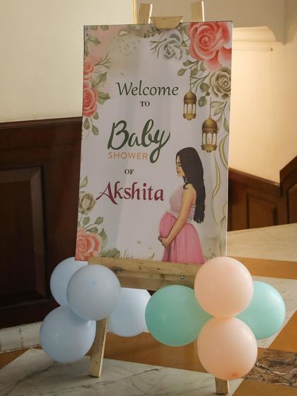 A personalized welcome board for a baby shower. The sign features a lovely illustration and is decorated with a few pastel-colored balloons for a gentle touch.