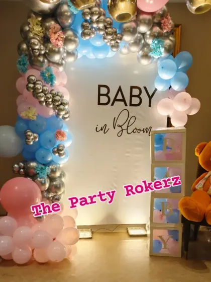 The full setup for the "Baby in Bloom" baby shower, including the balloon arch, backdrop, "BABY" blocks, and a large teddy bear.