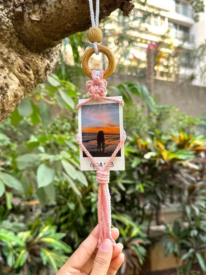 Our pink macrame polaroid holder hanging outdoors. This piece is perfect for adding a personal, handmade touch to your car, your room, or any small space.