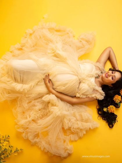 An artistic top-down shot. Lying on a bed of yellow, the flowing gown creates a beautiful floral shape, with flowers in her hair adding to the whimsical, sunny feel.