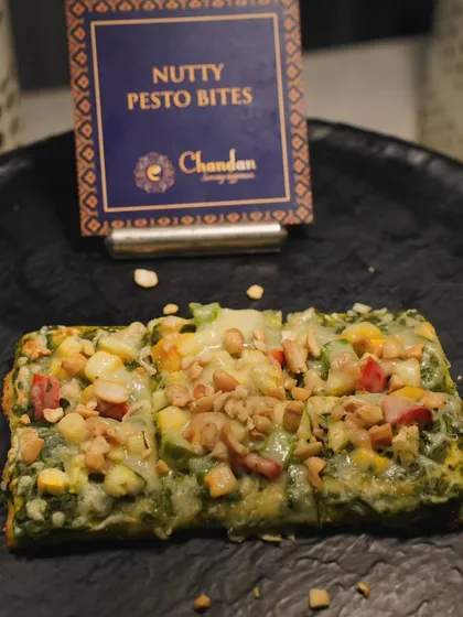 Nutty Pesto Bites. A savory flatbread topped with green pesto, assorted vegetables, and a sprinkle of nuts for a delightful crunch.