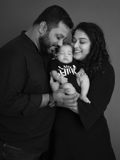 In this intimate black and white family portrait, the focus is entirely on the loving expressions and close connection between the parents and their sleeping newborn.