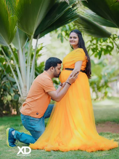 A classic and joyful pose with the father-to-be kneeling to kiss the baby bump in a sunny garden.