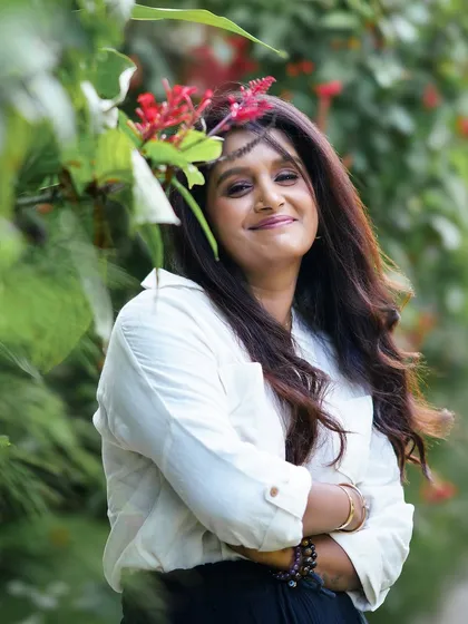 A warm and friendly portrait of a woman surrounded by red flowers and greenery, her smile lighting up the frame.