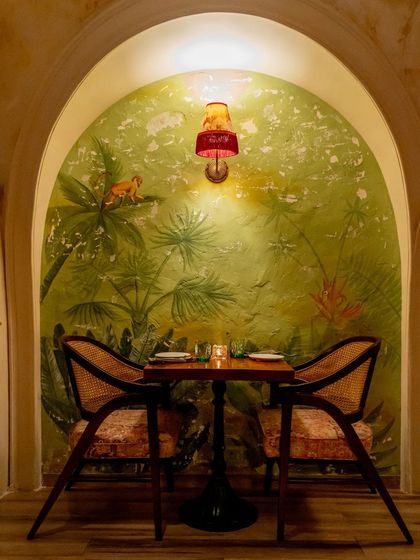 An intimate two-seater nook at Los Cavos, framed by a hand-painted tropical mural within a textured archway. This design choice creates cozy pockets within the larger space, perfect for quiet conversations.