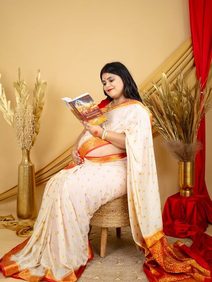 A peaceful moment of reflection. This mom-to-be, dressed in a classic white and red border saree, reads a spiritual book, adding a layer of personal meaning to her maternity session.