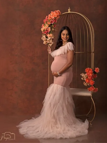 Standing beside the cage prop, this mother-to-be holds a bouquet, adding a touch of softness to the glamorous and powerful portrait.
