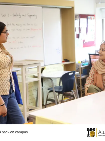 An alumna chats with a teacher in a classroom setting, demonstrating the comfortable and lasting relationships that are built here.