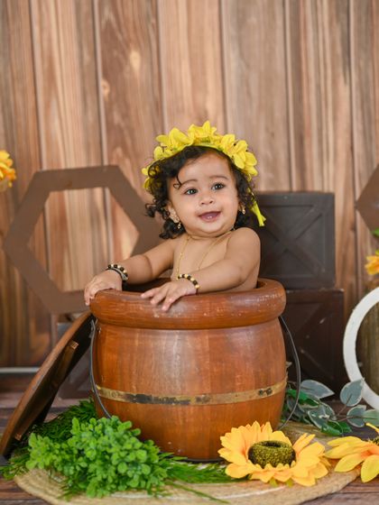 A sunflower-themed first birthday shoot. This little one is peeking out of a barrel, full of curiosity.
