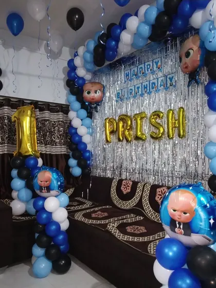 A Boss Baby theme for a first birthday, designed for a home setting. The blue, black, and white balloon arch is complemented by a silver foil curtain and character balloons.