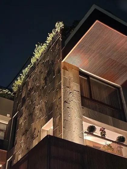 At the Ahluwalia Residence, the facade is a conversation between raw stone and finely detailed wood. At night, uplighting highlights this textural interplay, creating a dramatic and warm presence.