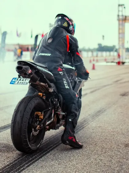 A rider on a black superbike prepares for launch, smoke coming from the rear tire as they warm it up for maximum grip.