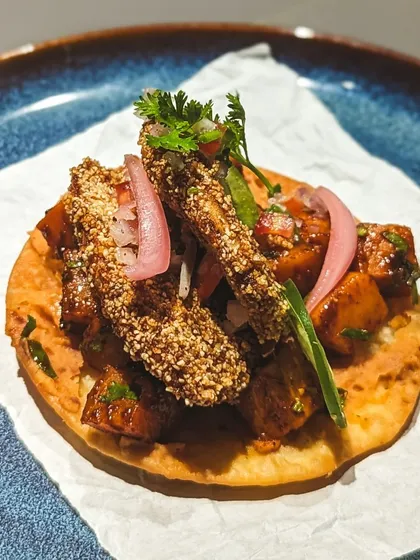 A tostada with cacao-crusted protein and pickled onions. This dish was a highlight of our dinner celebrating Mesoamerican flavors, demonstrating how cacao can be used as a savory spice rub to add depth and crunch.