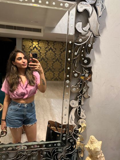 A mirror selfie in a casual summer outfit: a pink knotted shirt with denim shorts. It's a fun and easy look for a hot day.