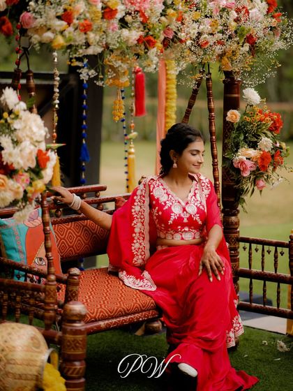 The beautiful bride seated on a traditional swing (oonjal) at her Mehendi, surrounded by flowers.