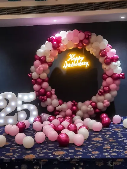 Celebrating a 25th wedding anniversary is a huge milestone, and this setup was designed to honor it. It includes a large balloon ring in shades of pink, a glowing 'Happy Anniversary' neon sign, and oversized light-up numbers for the perfect photo opportunity.