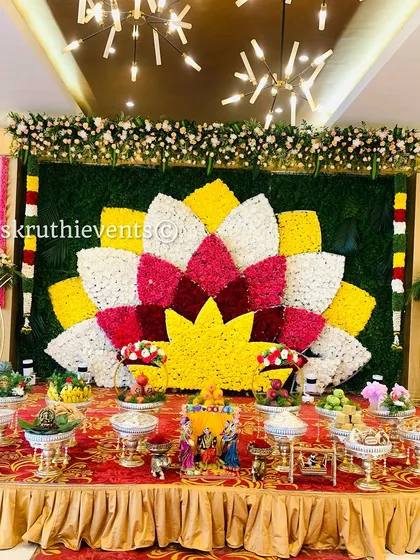 A stunning lotus-shaped backdrop made from petals of yellow, white, and pink flowers. This grand design, combined with a full display of offerings, creates a truly magnificent centerpiece for a baby shower.