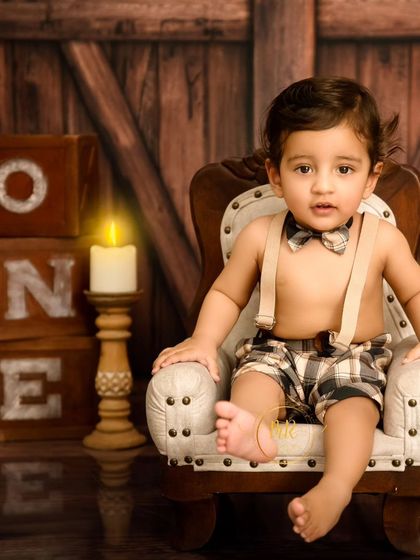 A handsome little boy sits in a miniature armchair, looking dapper in his bow tie and suspenders for his first birthday portraits.
