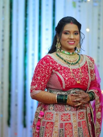 A smiling bride in a pink lehenga. She is wearing a green and pink Kundan choker set that perfectly picks up the colors in her outfit.
