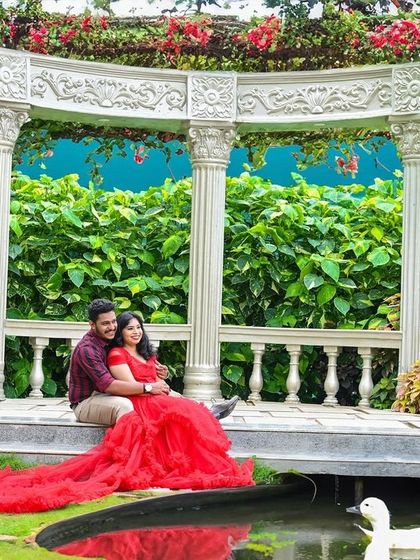 A stunning wide shot of a couple in a garden gazebo set, complete with a pond and swans. The bride's red gown creates a beautiful reflection.