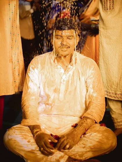 A candid moment from the groom's Haldi ceremony. He sits patiently as family members shower him with blessings and turmeric-infused water.