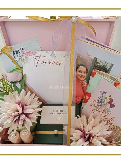 A thoughtful curation for a bride-to-be. This engagement hamper in a pink trunk includes a 'Forever' journal, a photo frame, and self-care items like a Nykaa face mask.