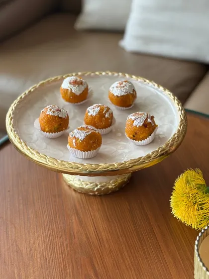 A classic golden cake stand with an intricate rope-textured edge. It provides a beautiful and elevated stage for serving desserts like these traditional motichoor ladoos during a festival.